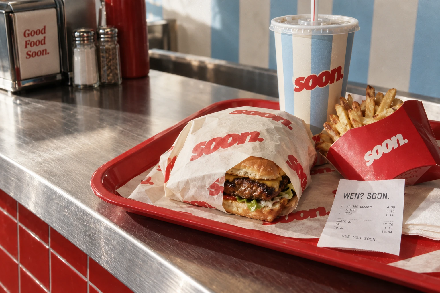 The soon. combo on a red tray at a real diner counter: square wrapped burger, fries, a striped cup and an order ticket